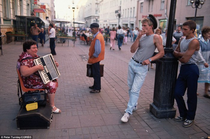 Женщина играет на популярной пешеходной улице Арбат в Москве, а несколько стоящих мужчин ее слушают.