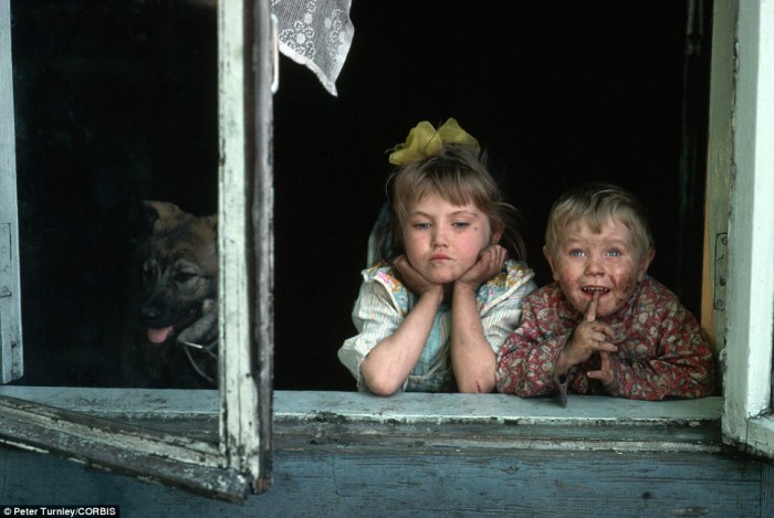 Двое детишек выглядывают из окна в горно-металлургическом городке в Сибири.