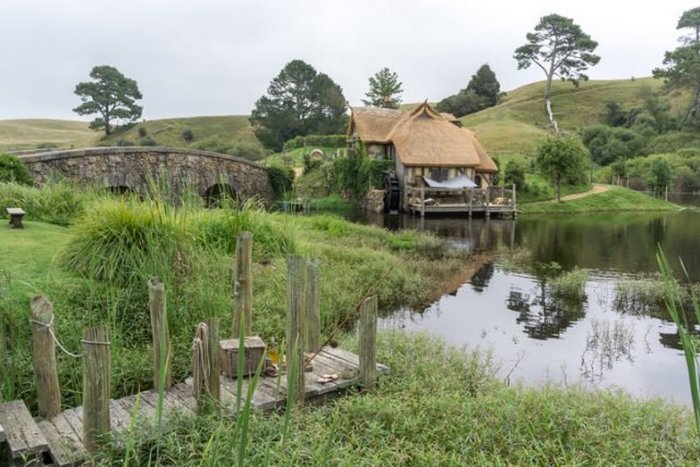 Мельница Хоббитона и двойной арочный мост, отражающиеся в озере. Новая Зеландия