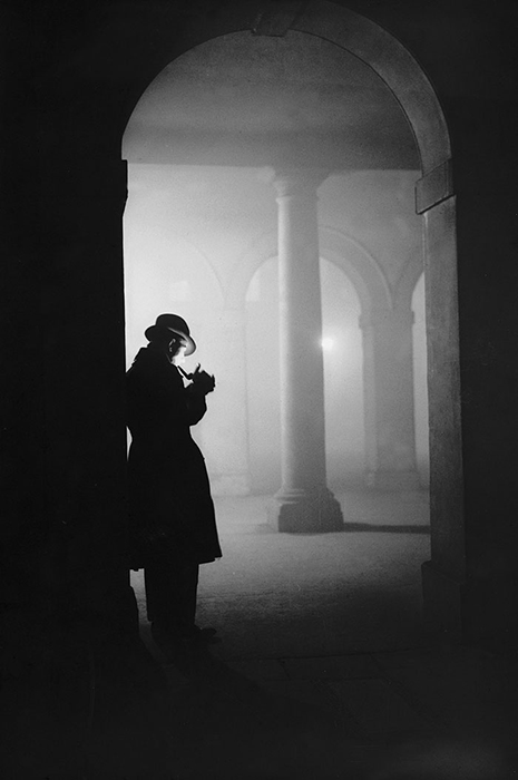 Мужчина курит трубку в тумане, стоя под аркой, 23 декабря 1935 года