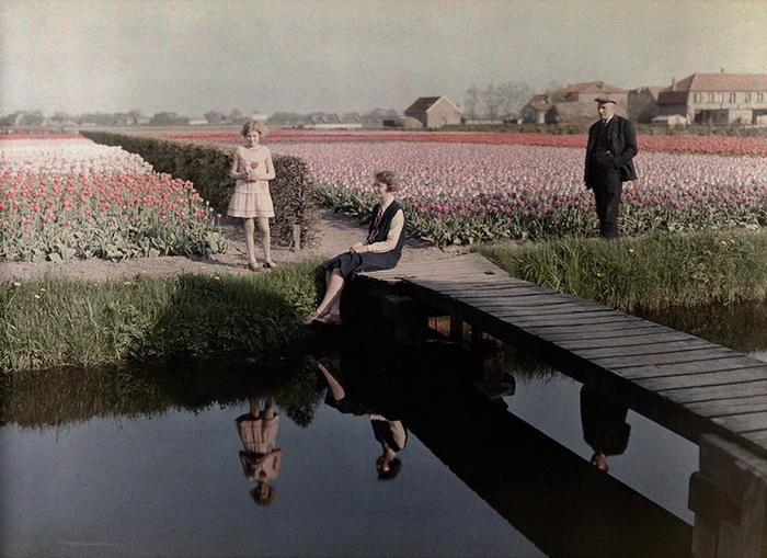Местные жители отдыхают возле канала, за ними простираются поля тюльпанов