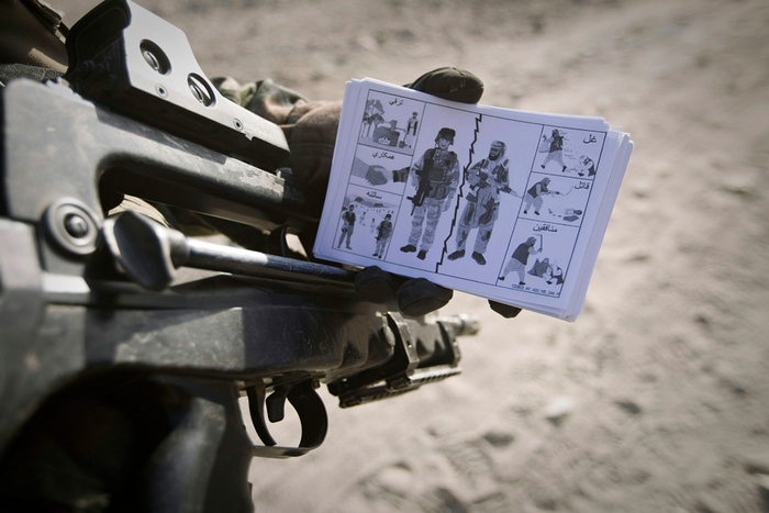Солдат с брошюркой для местных жителей с изображением разницы между солдатами и боевиками.