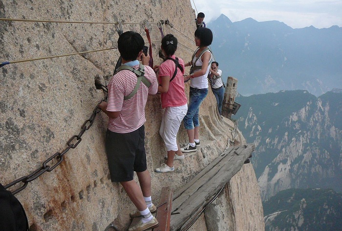 Туристы перемещаются по тонким, узким дощечкам на отвесной скале.