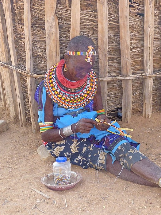Африканская женщина плетет сувениры из бисера.