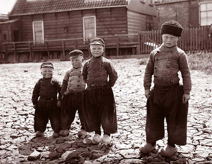 Четыре мальчика в мешковатых штанах, рубашках с пуговицами и в деревянных клогах на ногах. Волендам, Нидерланды.