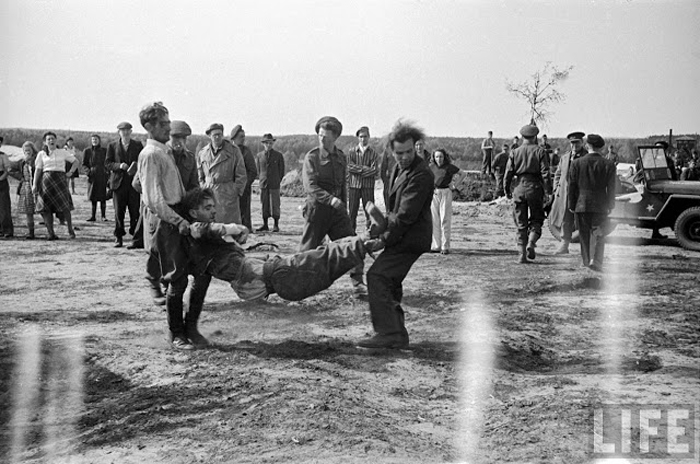Солдаты СС несут другого солдата, потерявшего сознание от обилия трупов, которых ему пришлось переносить в общую могилу.