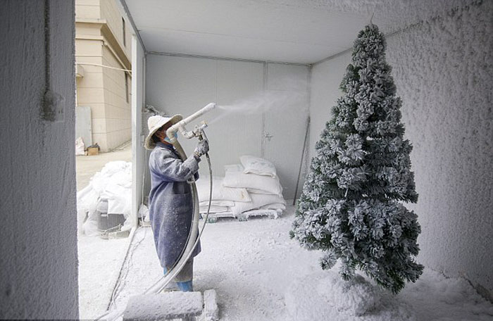 Рабочий покрывает елки искусственным снегом на заднем дворе фабрики.
