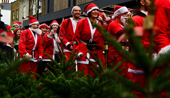 Санта Клаусы идут мимо точки продажи рождественских елок.