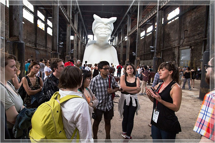 Посетители в Walker's  A Subtlety . На заднем плане видна белая скульптура, изображающая женщину в образе сфинкса.