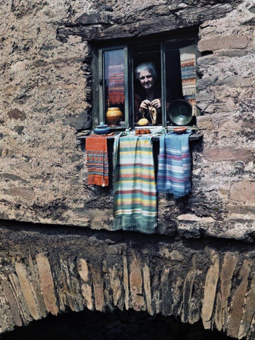 Женщина выглядывает из окна каменного дома в Эмблсайд, Лейк-Дистрикт (Озёрный край), Камбрия, Англия.