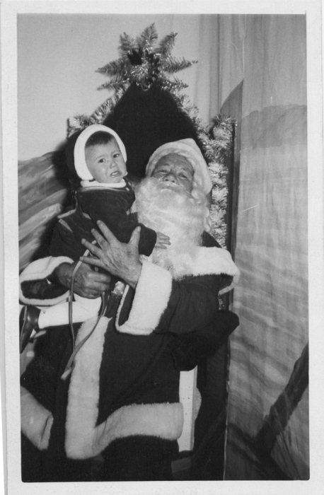Санта в короткой куртке, с черным поясом и пряжкой, восседает с мальчиком на троне.