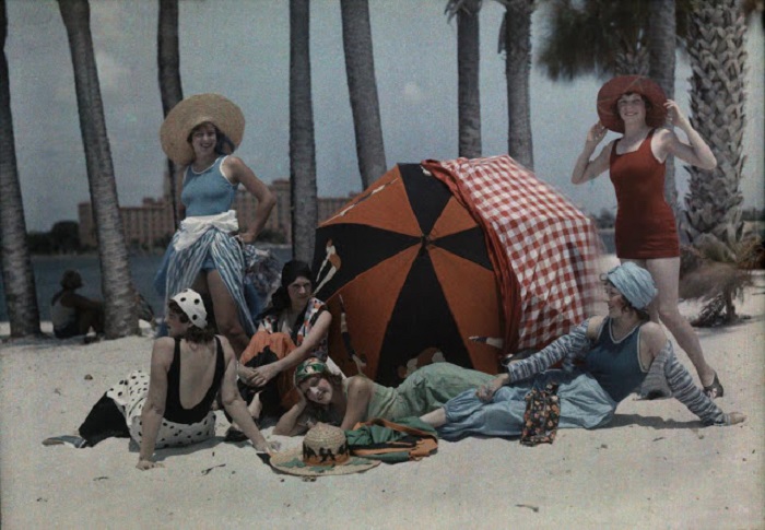 Красивые женщины позируют на пляже возле яркого зонтика.