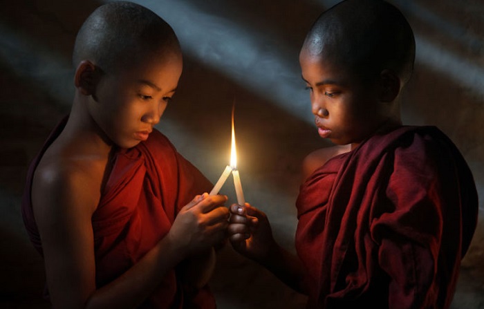 Молодые монахи зажигают свечи, чтобы помолиться.