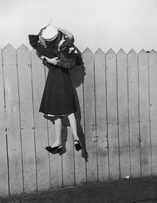 Моряк наклоняется через забор и поднимает девушку, чтобы поцеловать, 1945 год.