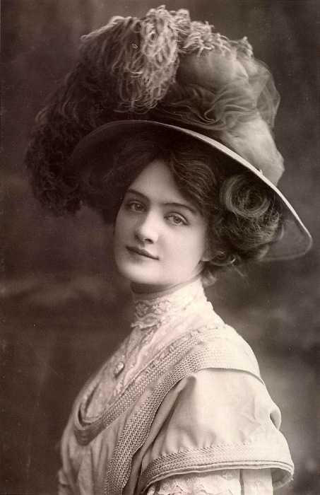 Девушка в шляпе с небольшими полями, украшенная тонкой прозрачной тканью и перьями.