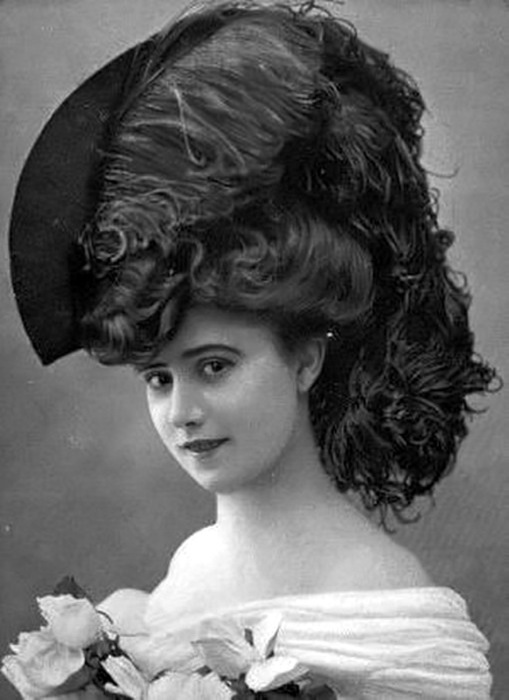Романтичный образ девушки в необычной шляпке, поля которой с одной стороны приподняты и украшены черным пером.