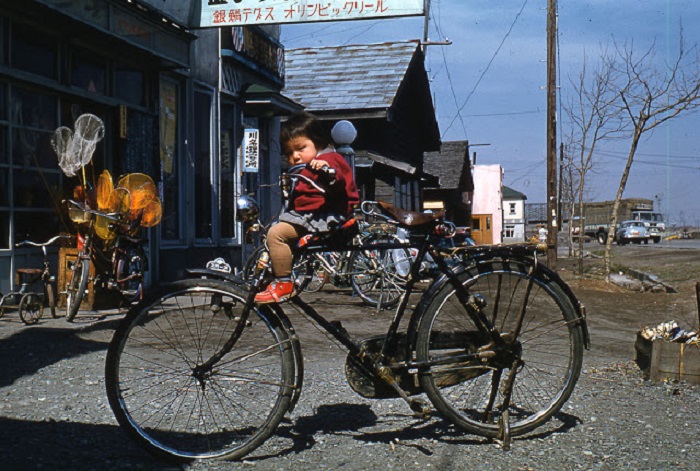 Маленькая девочка на большом велосипеде ожидает, когда же вернется мама из магазина рыболовных снастей.