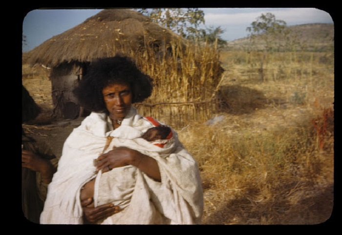 Женщина в белых одеяниях с ребенком на руках после родов.