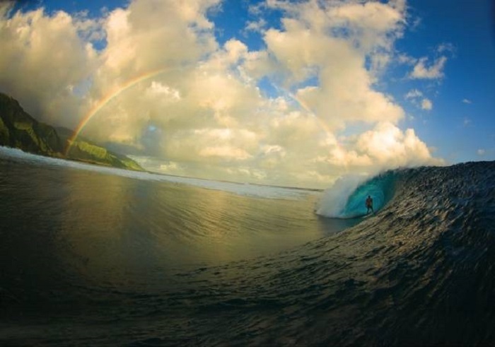 Серфер внутри волны на фоне радуги.