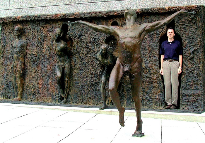Скульптура изображает одного человека, который отделяется от серой массы лиц, рук и ног.