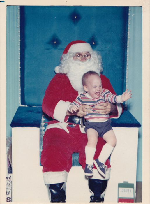 Санта-Клаус удерживает плачущего ребенка, который вырывается из его рук прямо к маме.