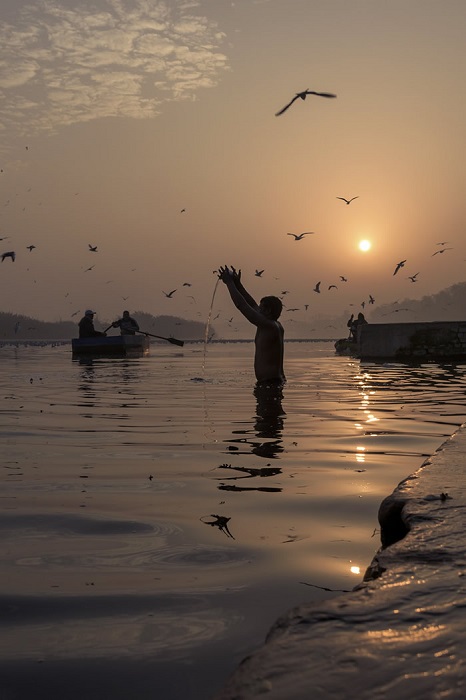 Верующий, который возносит молитву богу Солнца зимним утром у берега священной реки Джамна.  