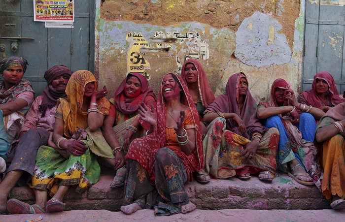 Индийские женщины, обсыпанные разноцветными красками, громко смеются, когда выполняется один из ритуалов празднества -  мужчин бьют бамбуковыми палками.