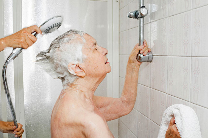 Дочка помогает маме принять душ, так как самостоятельно себя обслуживать пожилая женщина не может.