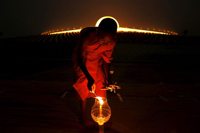 Буддийский монах зажигает свечу в храме на государственным праздником Маха Буча.