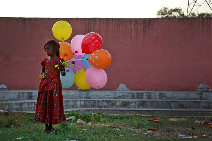 Девочка в национальном платье продает фрукты и шары на берегу реки Ямуна.