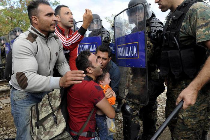 Мигрант с ребенком пытается пройти через полицейский заслон во время столкновений мигрантов с правоохранителями на греко-македонской границе.