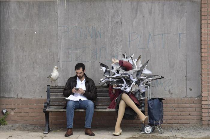 Мужчина сидит на скамейке рядом с одной из скульптур в тематическом парке в стиле арт-инсталляции британского художника Бэнкси.