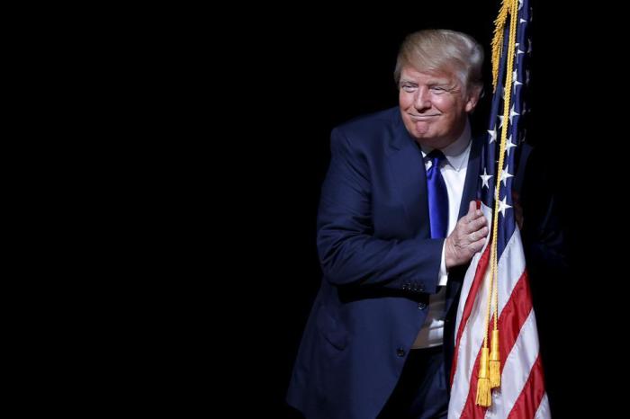 Республиканский кандидат в президенты обнимает американский флаг, выходя на сцену во время встречи с избирателями.