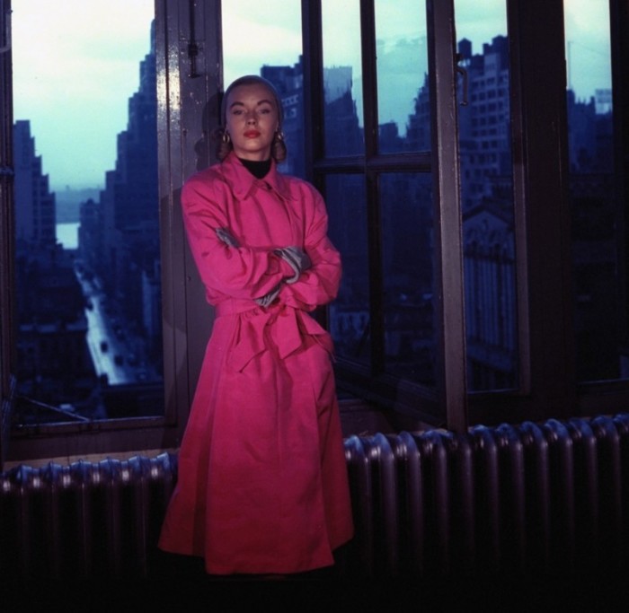 Модель в ярко-розовом плаще на фоне окна, выходящего на Манхэттен.