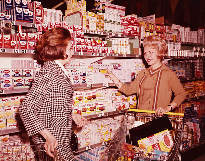 Две женщины выбирают товар, разложенный на полках. 1970 год.
