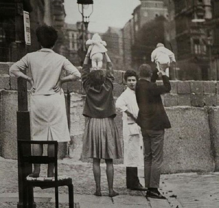 Молодые мама и папа показывают отпрысков своим родителям, а разделяет поколения возведенная Берлинская стена.