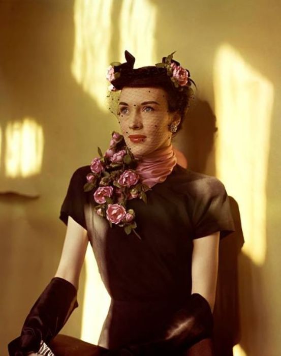 Образ модели состоит из черного платья с коротким рукавом, декорированной шляпки с вуалью и шелкового шарфа с розами.