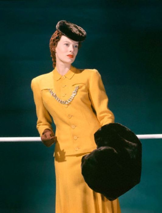 Девушка-модель в желто-золотом твидовом костюме, декорированном массивной цепочкой.
