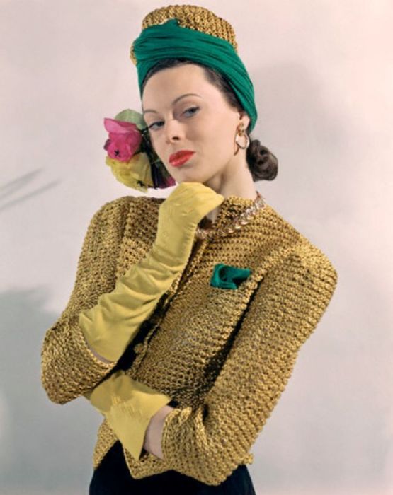 Модель в необычном головном уборе – золотом вязаном тюрбане, дополненным желто-розовыми цветами и зеленым платком.