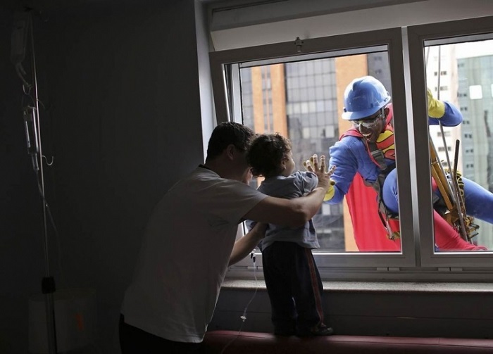 Мужчина в костюме Супермена улыбается 2-летнему пациенту Жоао Бертола и его отцу в больнице IInfantil Sabara в Сан-Паулу, Бразилия.