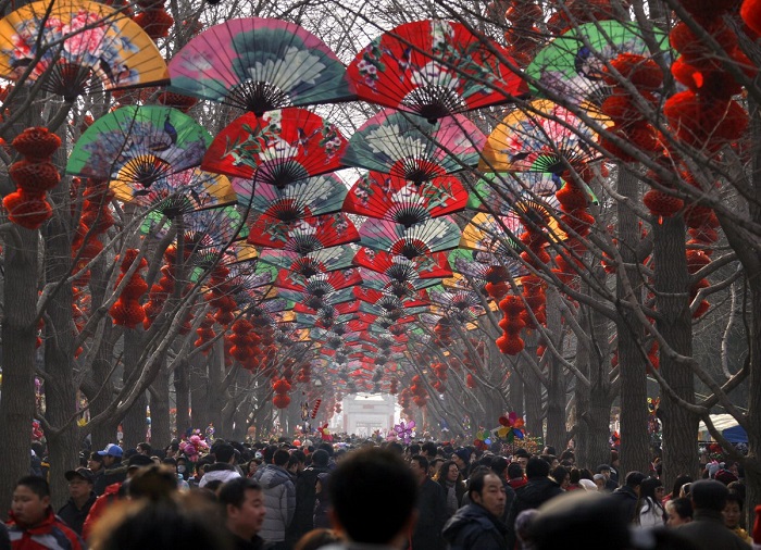 Толпы людей ходят среди деревьев, украшенных красными фонарями на храмовой ярмарке в честь празднования китайского Нового года в Пекине.