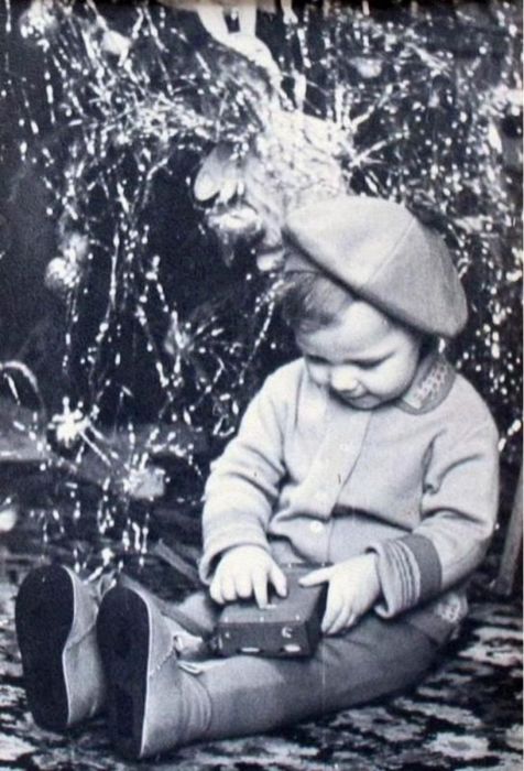 Ребенок рассматривает новогодний подарок прямо под елкой. 1960 год.