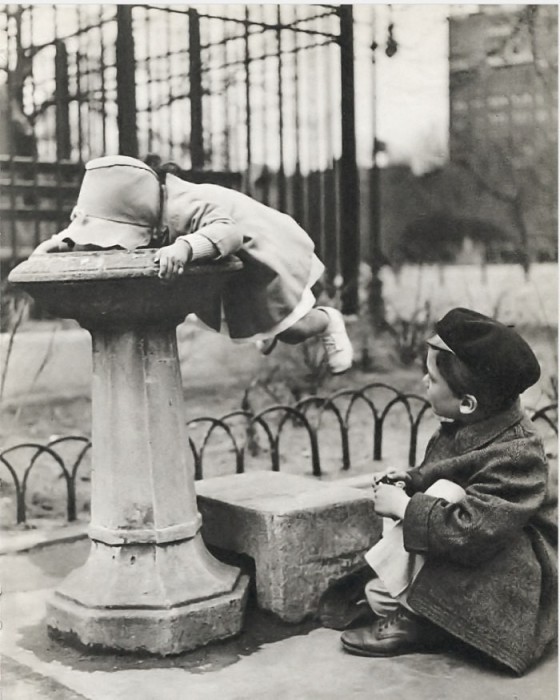 Маленькая девочка пьет из фонтана воду.