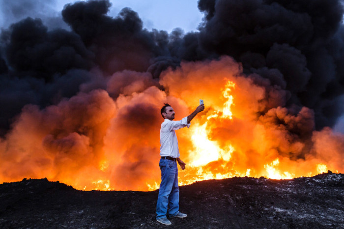 Мужчина делает фотографию напротив пожара от нефти.