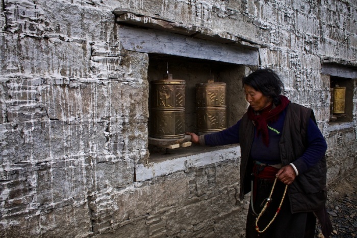 Старая тибетская женщина поворачивает цилиндры, которые сделаны из позолоченной бронзы и покрыты буддийскими надписями и символами, произнос я мантру Ом Мани Падме Хум.