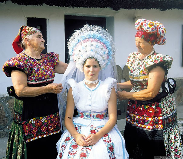 Свадебное платье состоит из цветочных узоров, которые выполнены из трех ярких цветов, а в головной убор вплетаются колоски пшеницы.