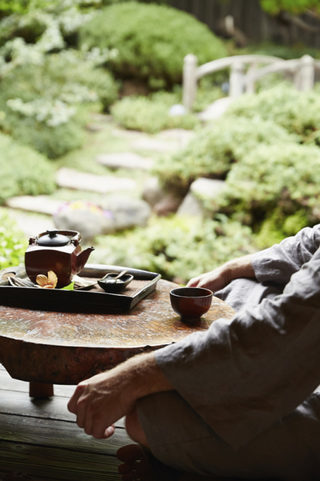 Мужчина в халате пьёт чай в саду.