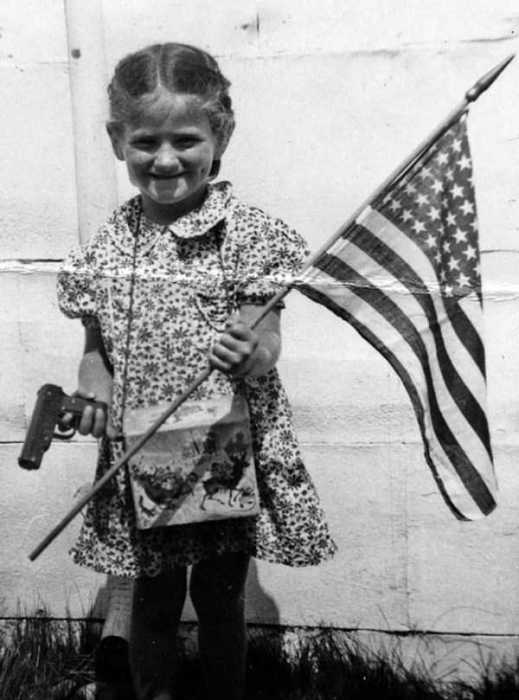 Шестилетняя девочка с американским флагом и пистолетом в руках.