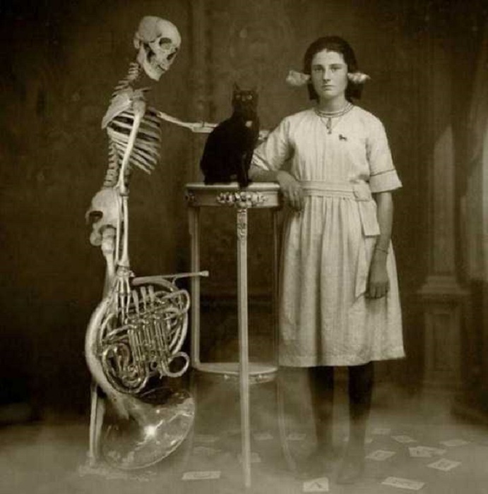 Винтажная фотография девочки и скелета из шкафа с черным котом по середине.