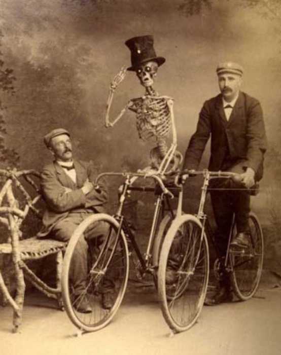 Скелет в цилиндре на велосипеде отдающий честь.